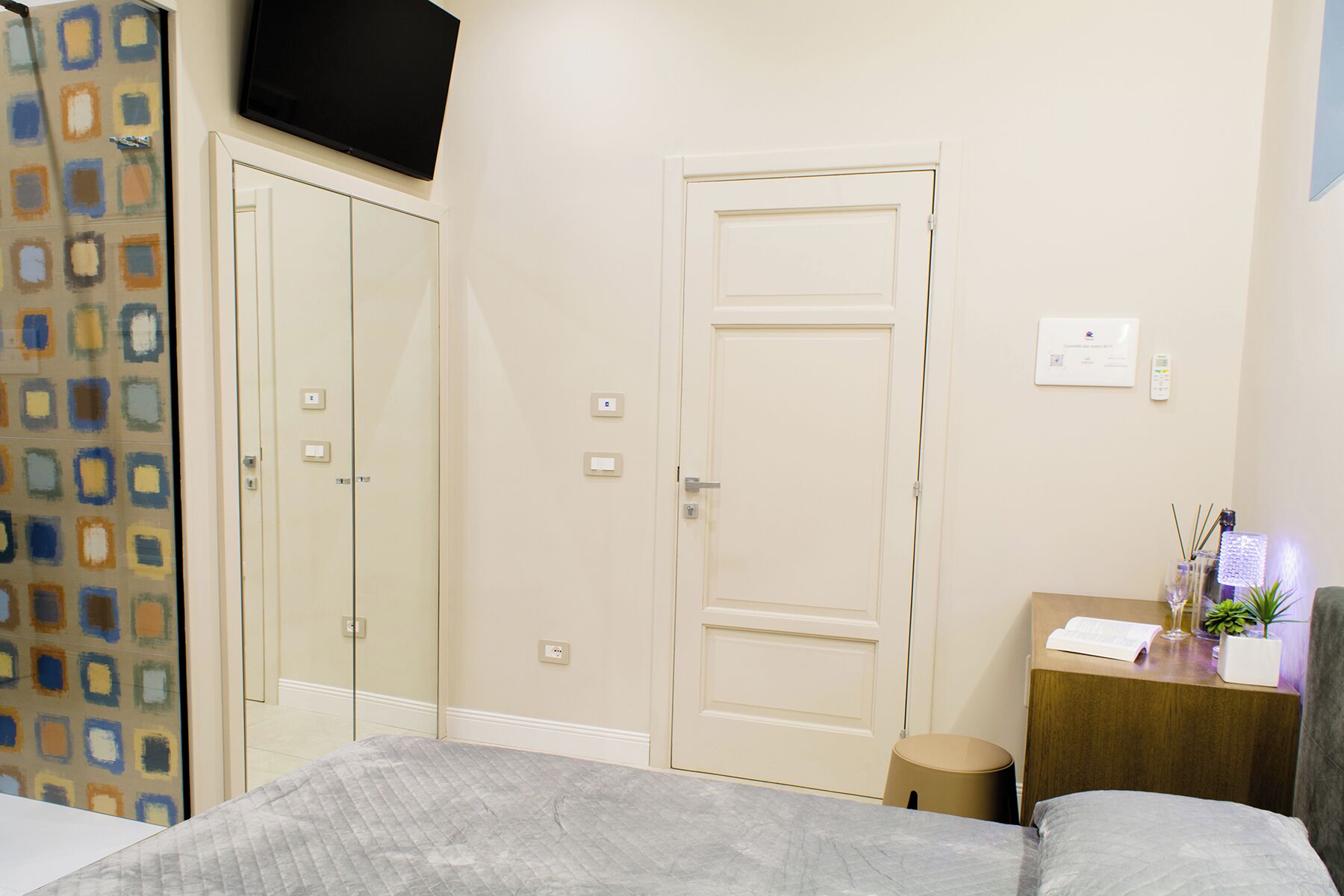 A hotel room with a bed, a desk with a plant, a TV, and a door.