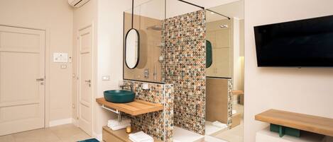 A modern bathroom with a large mirror, a round sink, a shower enclosure, and a flat-screen TV mounted on the wall.