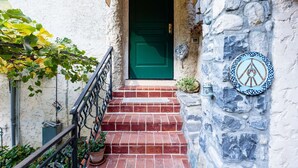 Un mur de pierre orné d’une plaque décorative, une porte verte et un escalier en briques menant à l’entrée d’un bâtiment.