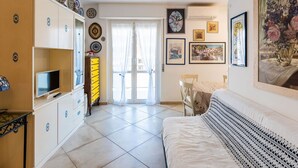 Ein Zimmer mit einem Bett, einem Fernseher, einem gelben Schrank und einer Tür, die auf einen Balkon führt.