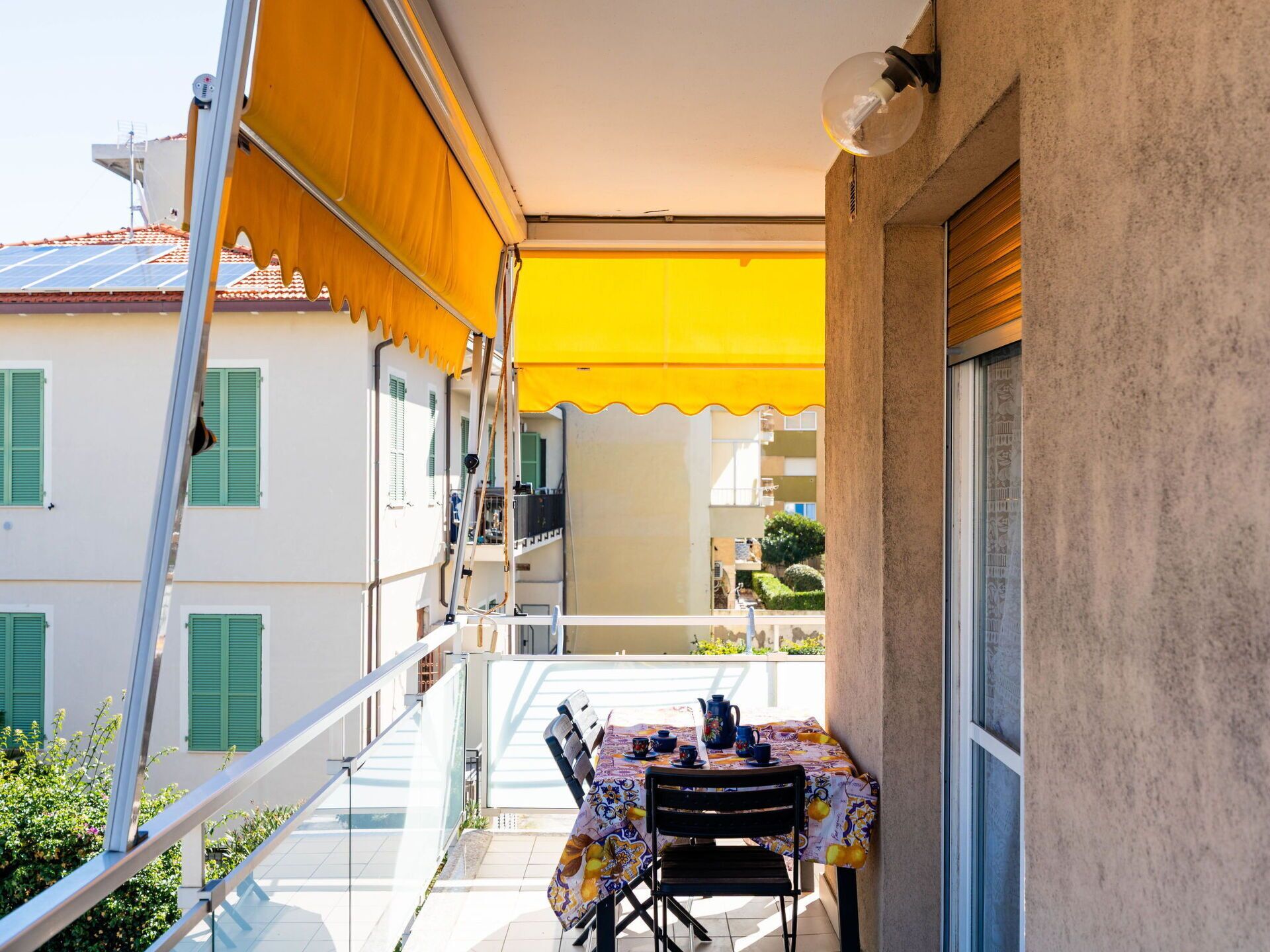 A balcony with a table set for two, a yellow awning, and a view of neighboring buildings.