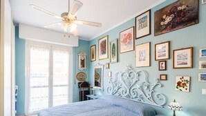 Ein Schlafzimmer mit Bett, Nachttisch, Schminktisch, Deckenventilator und einer Wand mit gerahmten Bildern.