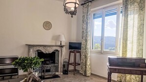 Una sala de estar con chimenea, un televisor sobre un mueble bajo, una planta en maceta y vistas al exterior a través de una ventana.