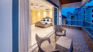 A balcony with wicker furniture, a bed with a headboard, and a view of a building under construction. - Dancenter Avanora Villa (Arpora)