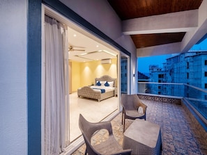 A balcony with wicker furniture, a bed with a headboard, and a view of a building under construction. - Dancenter Avanora Villa (Arpora)