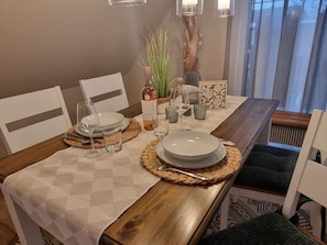 Une table à manger dressée avec des assiettes, des verres et une bouteille, entourée de sets de table en fibres tressées et de chaises.