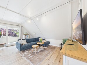 Et moderne loftværelse med skrå vægge, et stort vindue, en seng, et skrivebord og et fjernsyn.