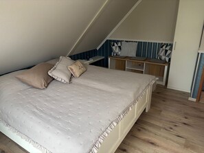 Une chambre avec un plafond en pente, un lit à volants, un bureau avec une chaise et un mur décoré de motifs.