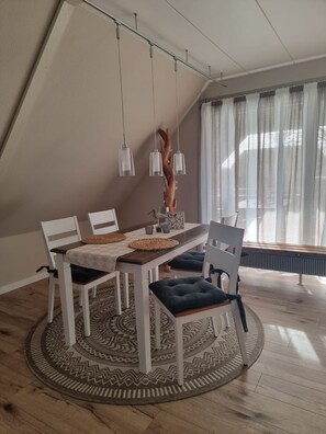 Un espace repas avec une table ronde, des chaises blanches, un tapis à motifs et des luminaires suspendus.