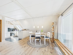 A modern kitchen with white cabinets, a dining area with a round table and chairs, and a large window with blinds.