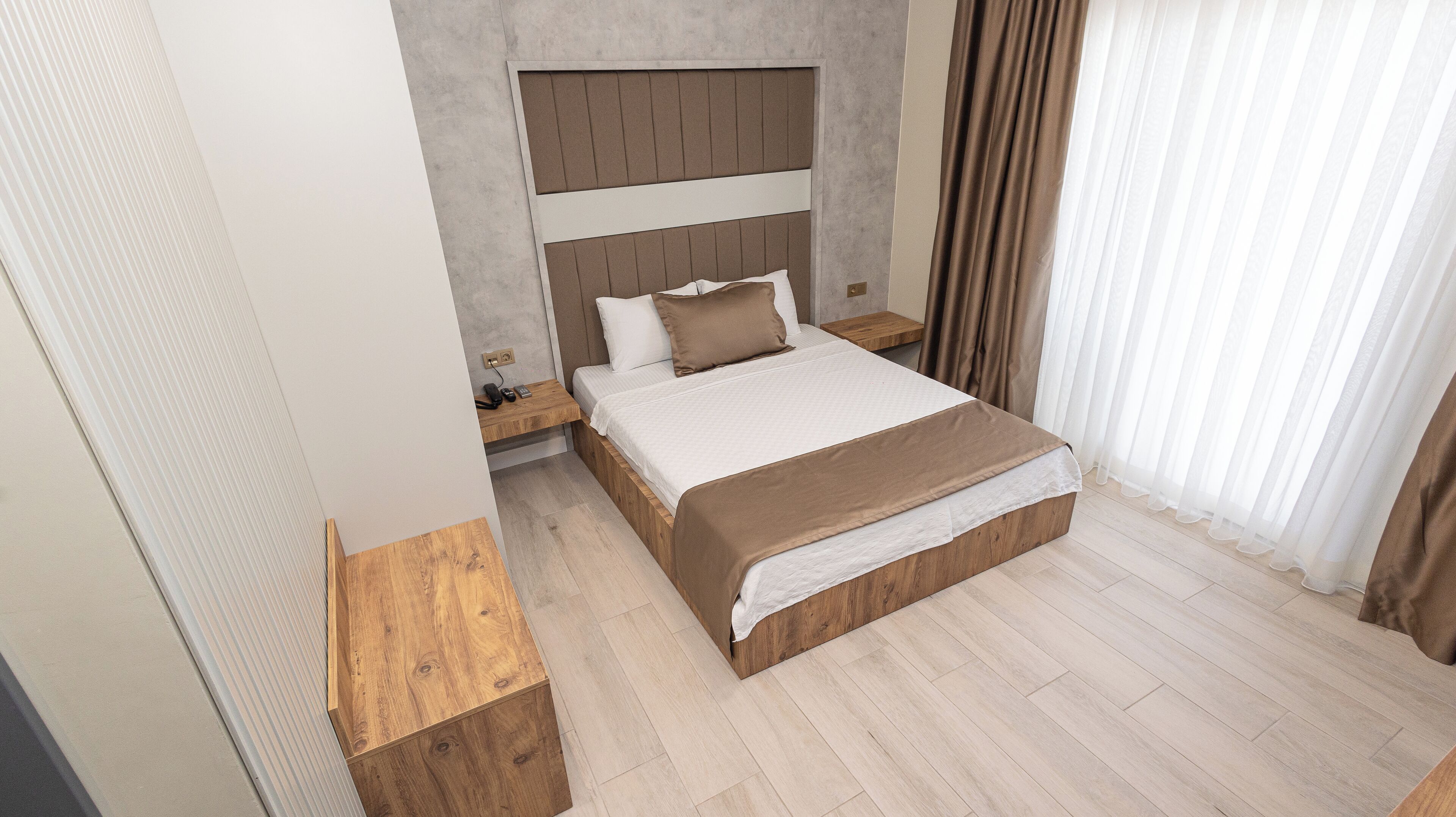 A bedroom with a wooden headboard, a bed with white and brown bedding, a bedside table, and a nightstand.