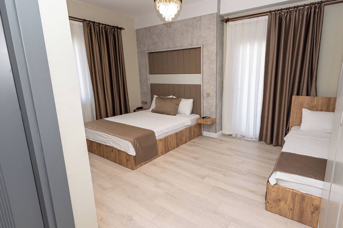 A modern hotel room with two beds, a wooden headboard, a bedside table, and a large window with curtains.