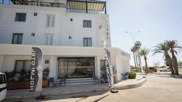 Un hotel con fachada moderna, mobiliario exterior y palmeras.
