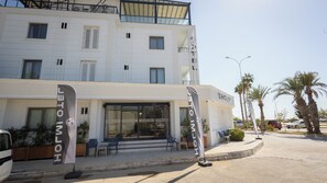A hotel with a modern facade, outdoor seating, and palm trees. - HOLMİ OTEL (Taşucu)