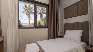 Una habitación de hotel con una cama, una mesita de noche, una ventana con cortinas y vistas a palmeras.