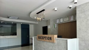A reception desk with a sign, a modern kitchen area, and a polished floor. - HOLMİ OTEL (Taşucu)