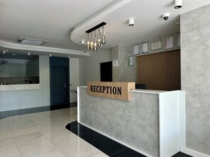 A reception desk with a sign, a modern kitchen area, and a polished floor. - HOLMİ OTEL (Taşucu)