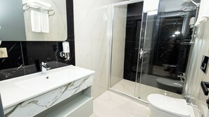 A modern bathroom with a marble sink, a glass-enclosed shower, and a toilet. - HOLMİ OTEL (Taşucu)