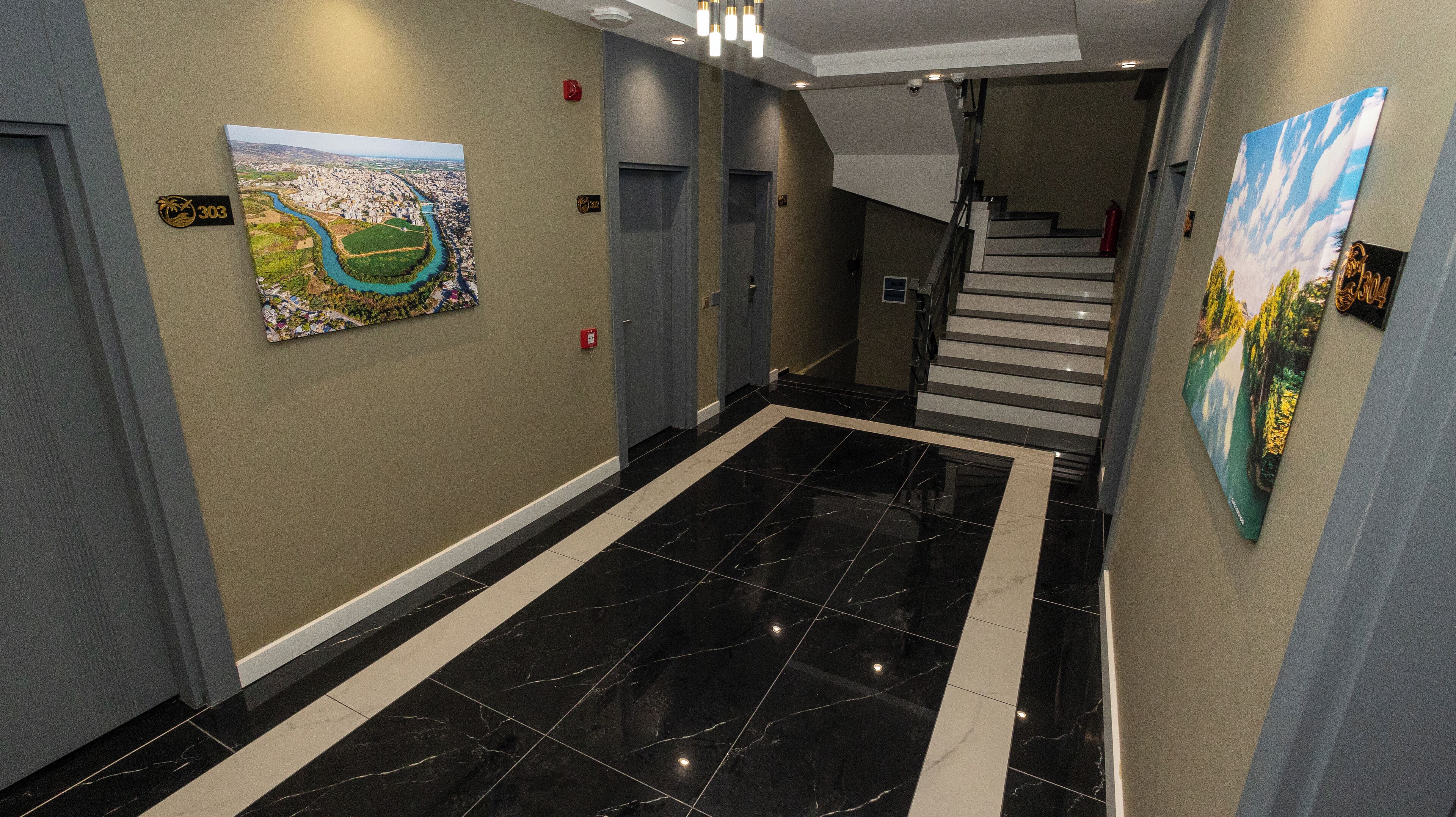 A hallway with a black and white tiled floor, a staircase, and two paintings on the walls.