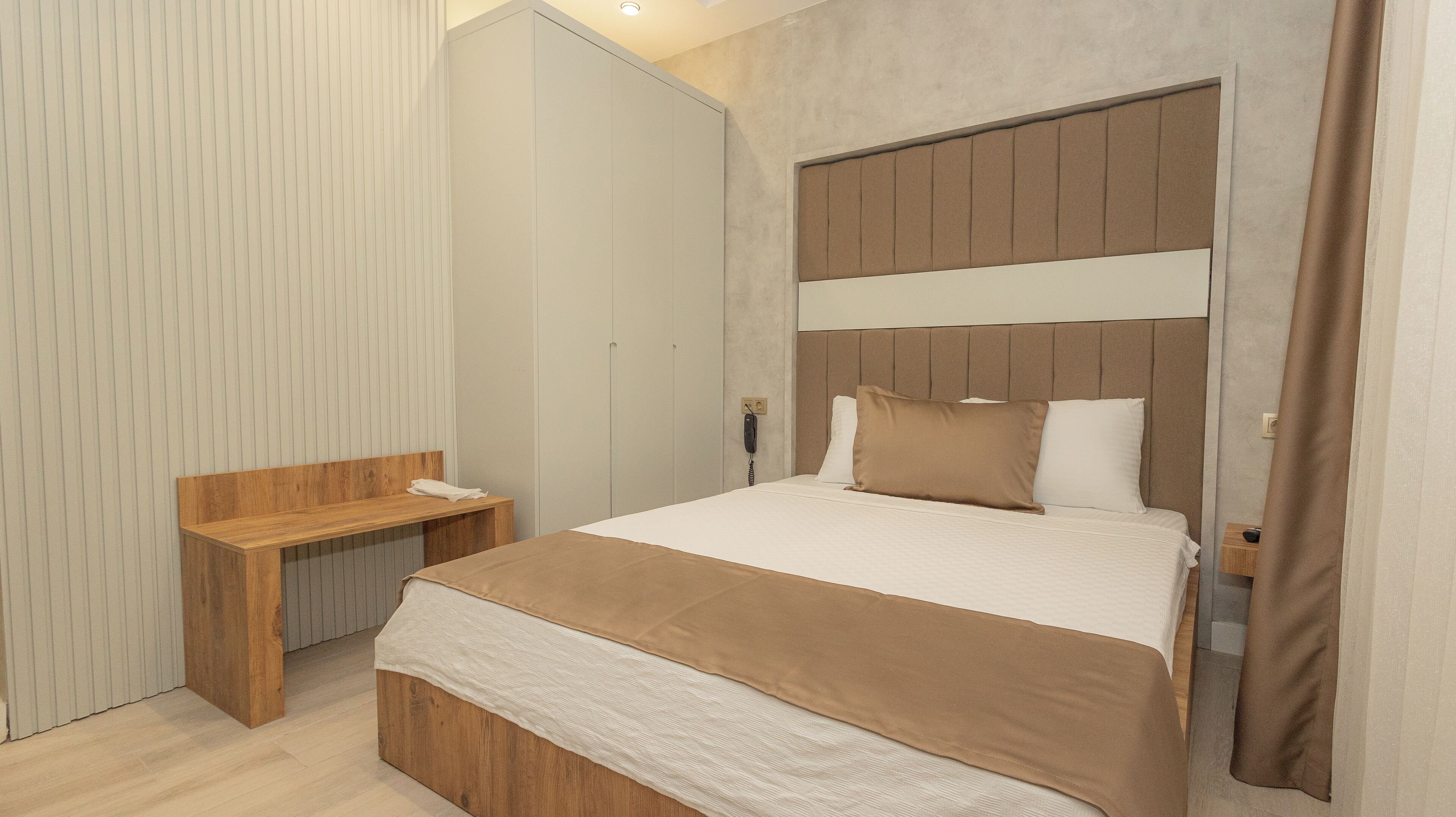 A modern bedroom with a large bed, a wooden bench, and a telephone on the wall.