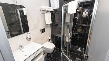 A modern bathroom with a glass-enclosed shower, a white sink, and a toilet.