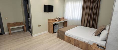 A hotel room with a bed, a desk with a TV, a small fridge, and a bench.