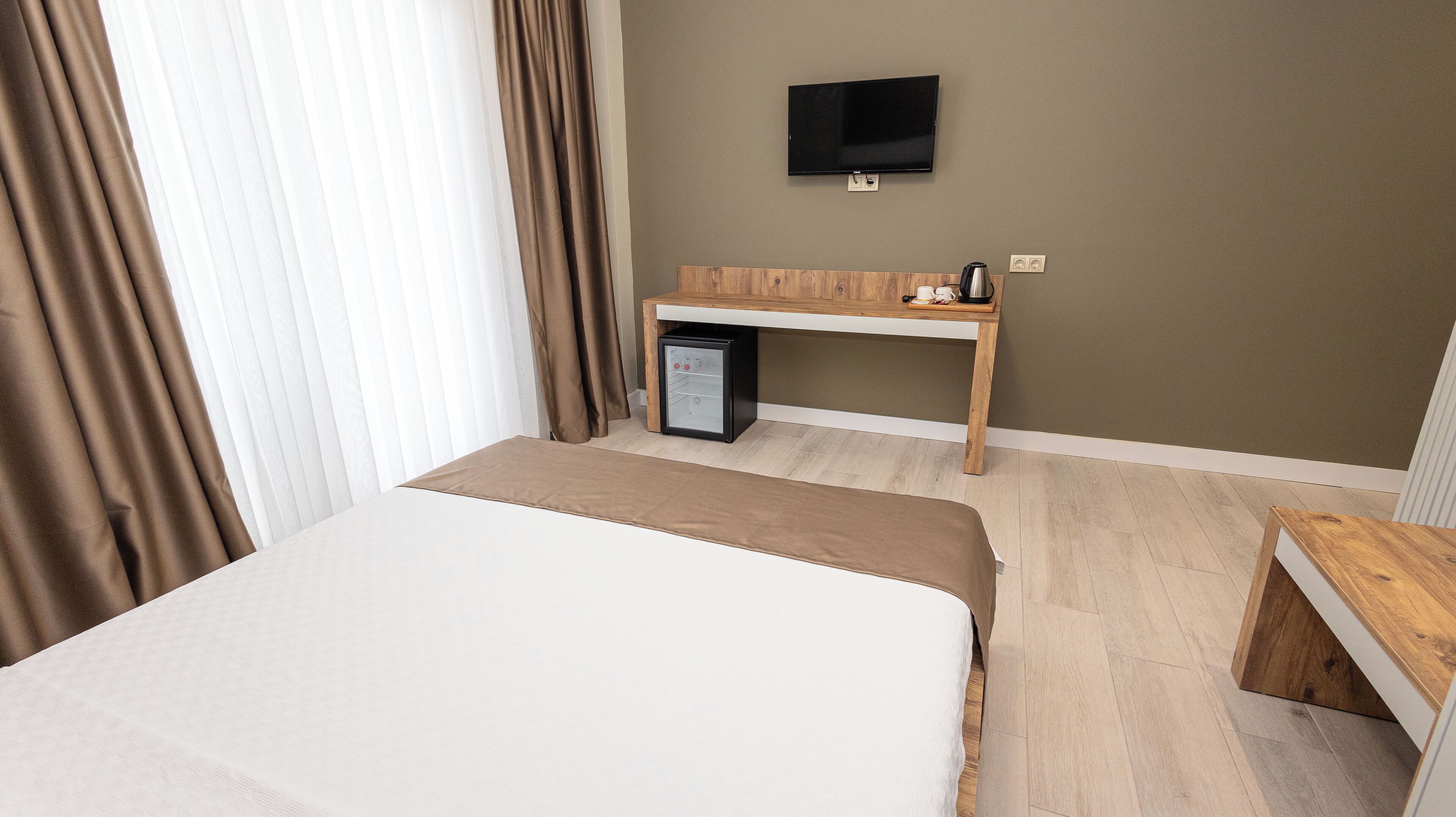 A hotel room with a bed, a desk with a coffee maker, a TV, and a mini-fridge.