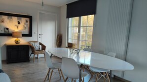 Un comedor moderno con una mesa blanca, cuatro sillas, un armario negro y una lámpara.