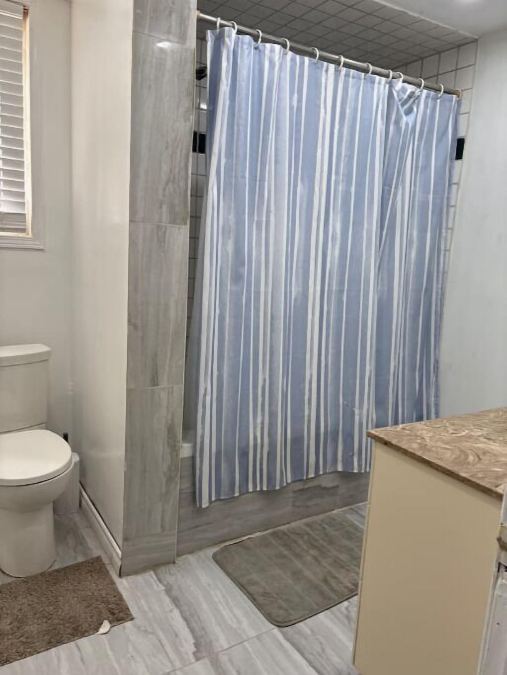 A bathroom with a shower curtain, toilet, and a sink area.