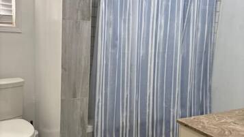 A bathroom with a shower curtain, toilet, and a sink area.