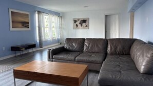 A modern living room with a leather sectional sofa, a wooden coffee table, and a world map artwork on the wall. - Beautiful Riverfront House (Campbellford)