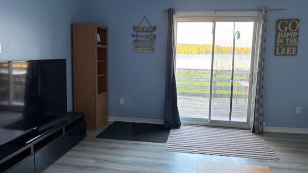 A living room with a TV, a wooden cabinet, a sliding glass door to a backyard, and a motivational sign on the wall. - Beautiful Riverfront House (Campbellford)