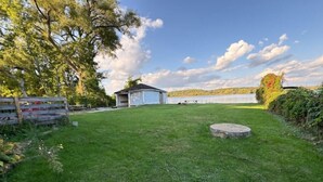 A grassy backyard with a small shed, a wooden fence, and a stone well. - Beautiful Riverfront House (Campbellford)