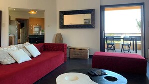 A modern living room with a red sofa, a white ottoman, and a black coffee table. There is a large mirror on the wall and a view of the balcony with outdoor furniture. - 140 m2 sea view and private mini pool 9 (Propriano)