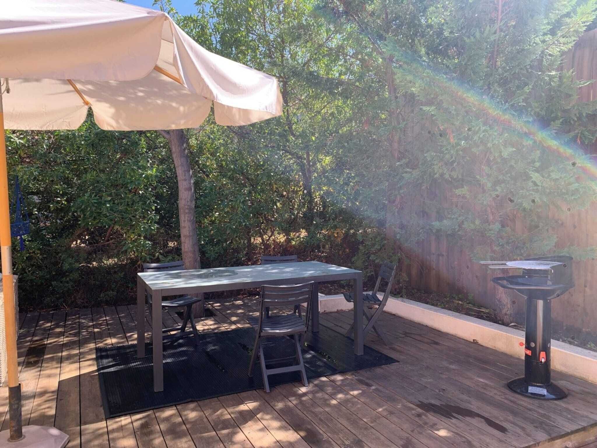 Una terraza de madera con una mesa, sillas, una sombrilla y una parrilla de barbacoa.