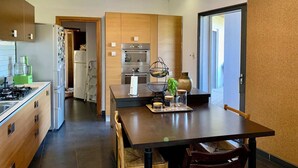 A modern kitchen with wooden cabinets, a gas stove, a refrigerator, and an oven. There is a dining table with chairs and a hanging light fixture above. - 140 m2 sea view and private mini pool 9 (Propriano)