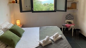 A bedroom with a large bed, a window with a view of greenery, a chair with a patterned cushion, and a bedside table with a lamp. - 140 m2 sea view and private mini pool 9 (Propriano)