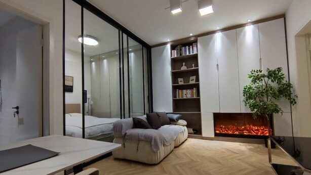 A modern bedroom with a glass partition, a sofa, a fireplace, and a bookshelf.