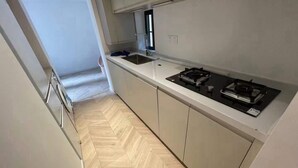 A narrow kitchen with a herringbone floor, white cabinets, and a gas stove.