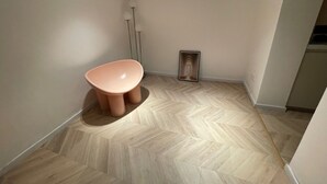 A small, modern bathroom with a herringbone-patterned floor, a pink chair, and a framed picture on the wall.