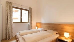 A bedroom with two beds, a window with curtains, a bedside table with a lamp, and a wooden headboard. - Verwall Apartment 3 (Tschagguns)