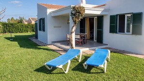 Una villa moderna con un patio, dos sillones de descanso y una zona de comedor.