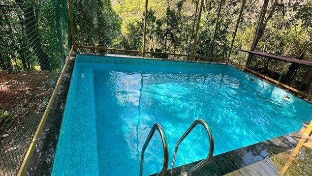 A rectangular swimming pool with clear blue water, surrounded by a wooden deck and a metal safety railing. - Green Breeze Resort (Dapoli)
