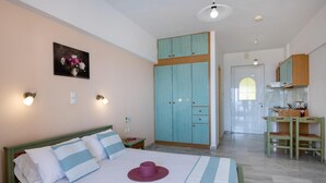 A bedroom with a bed, a nightstand, a dresser, a wardrobe, a desk with a chair, and a kitchen area. - Studio Apartment '1 Two Adults' with Sea View, Shared Pool and Wi-Fi (Sfakaki)