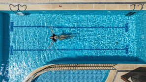 Una piscina rectangular con agua azul cristalina, un trampolín y una zona de solárium con baldosas.