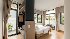 Un dormitorio moderno con cama, armario de madera, una mesita y balcón con vistas a zonas verdes.