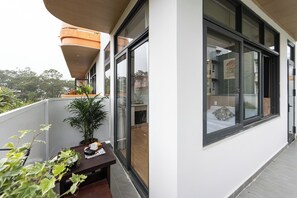 A balcony with a potted plant, a small table with a teapot, and a window with a bed visible inside. - Almira Home Da Lat (Cam Ly - Da Lat)