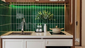 Una cocina compacta con un lavamanos, un refrigerador Hisense, un mueble de madera con puertas de vidrio y un salpicadero con azulejos verdes.