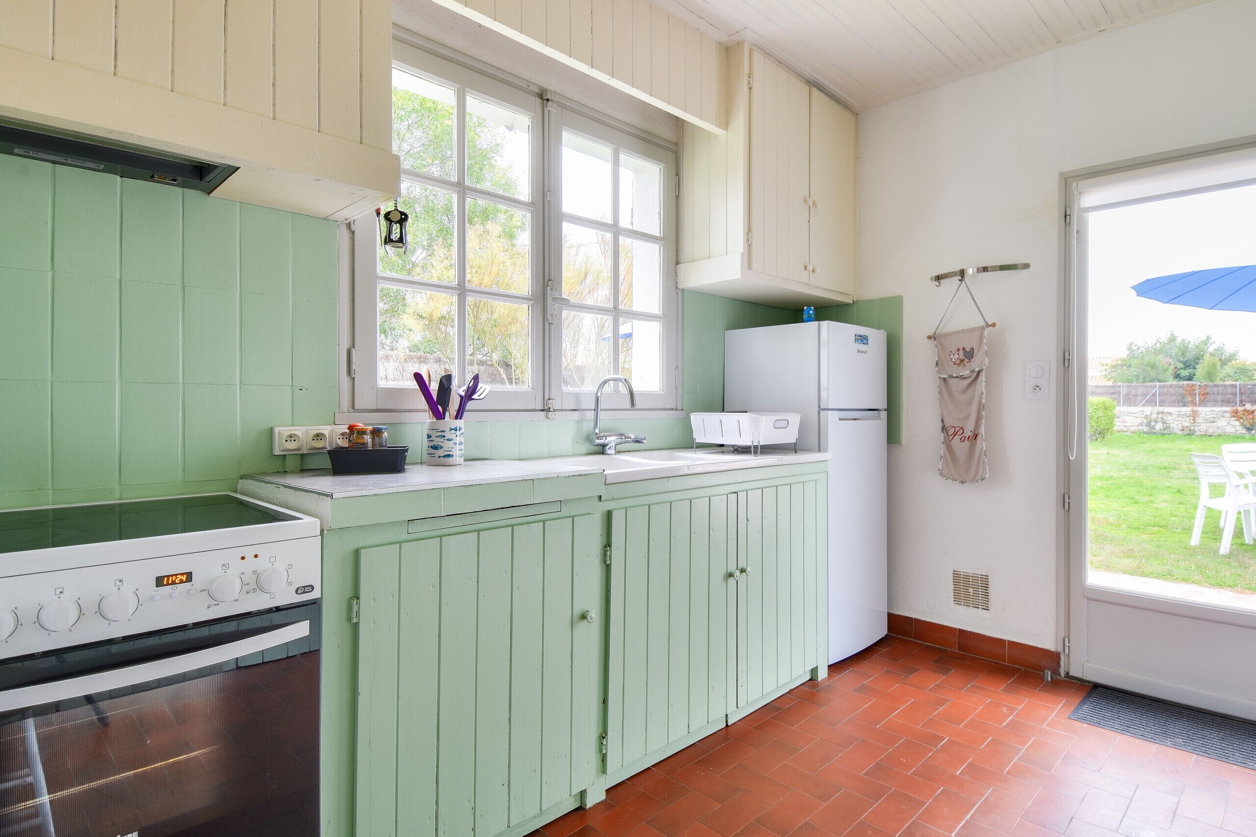 A kitchen with green cabinets, a white stove, and a window with a view of the outdoors.