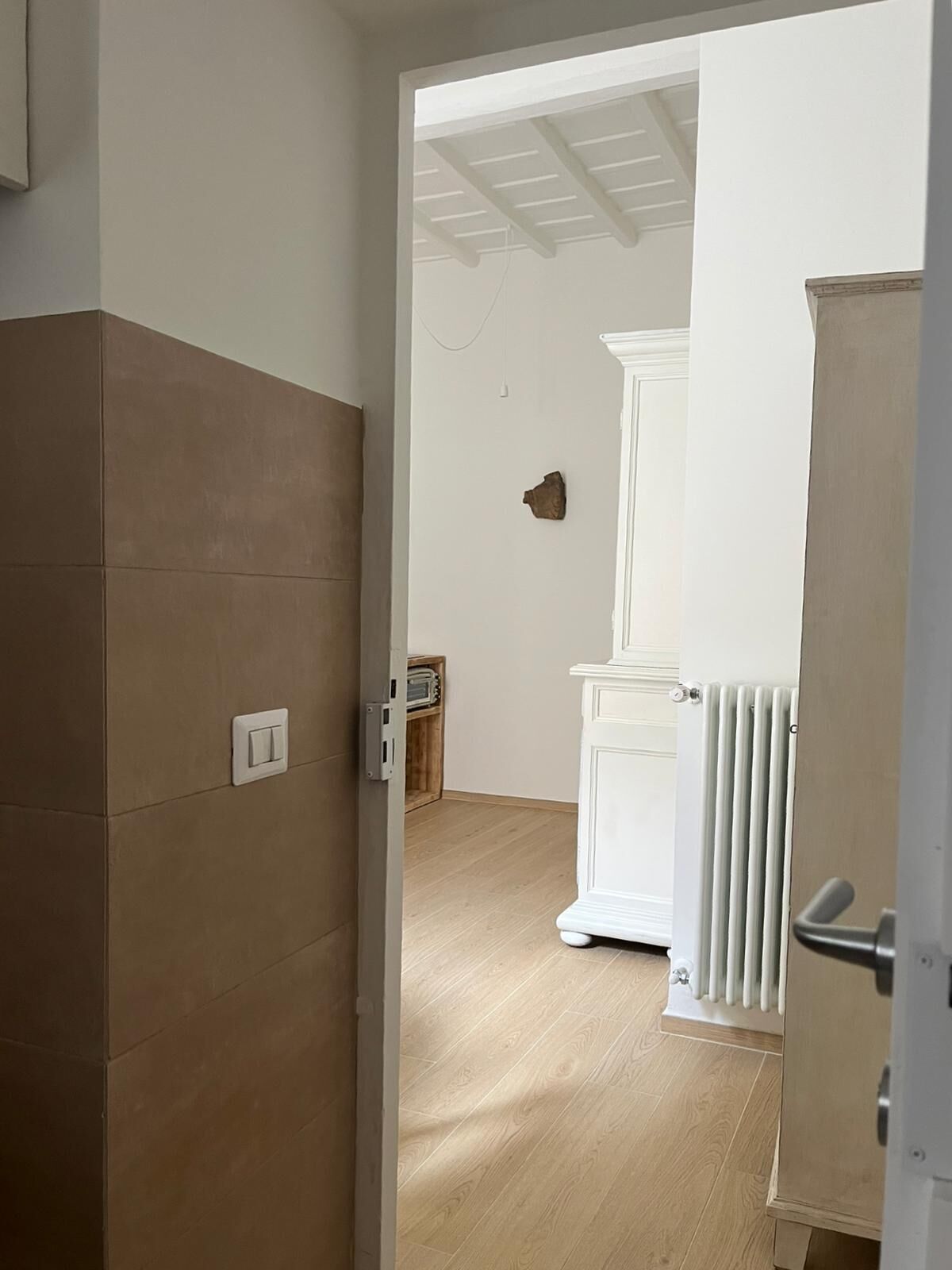 Ein Zimmer mit Holzboden, einem weißen Heizkörper und einer Tür zu einem anderen Raum.